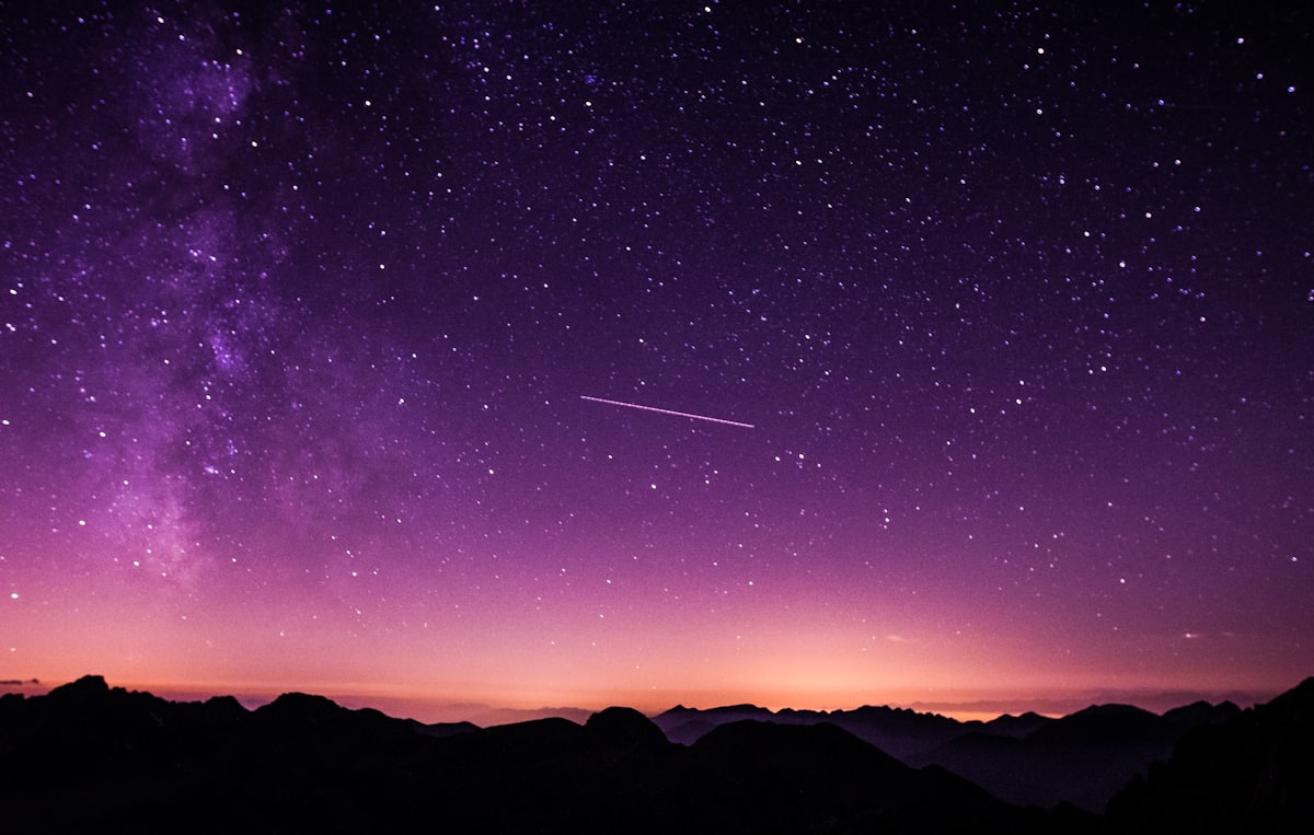 A shooting star crossing the Milky Way above dark mountains