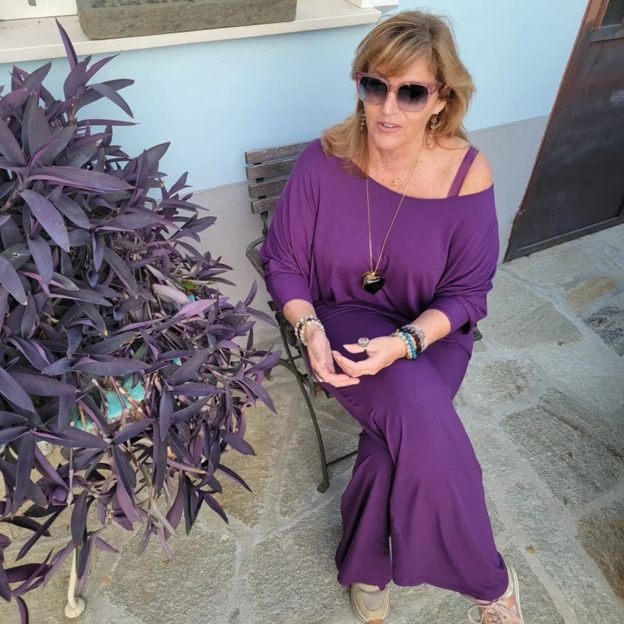 Catherine Regan, founder of Mystic Indigo Universe, seated outdoors beside a purple wandering-jew plant.