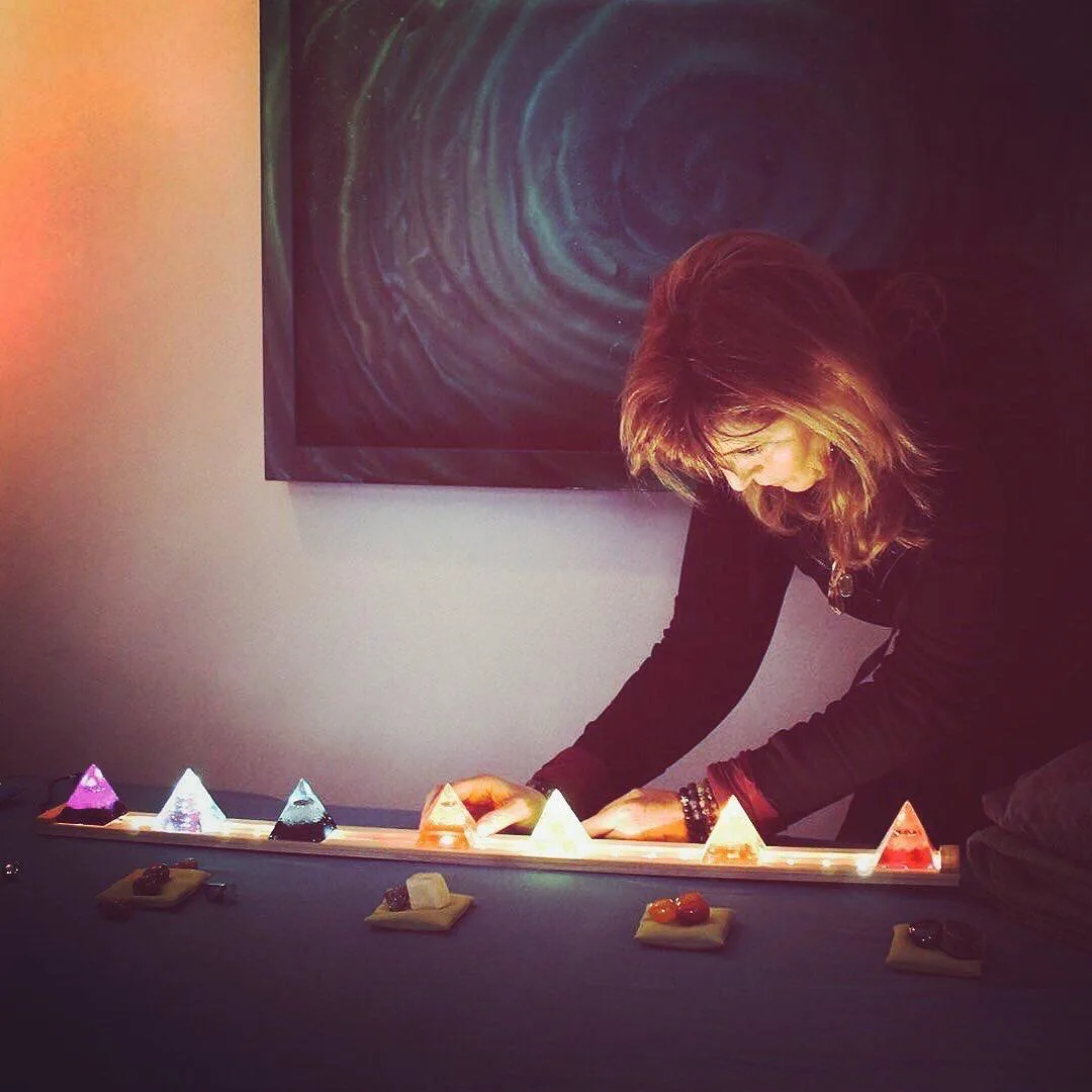 Catherine arranging seven lit crystal pyramids in chakra colors along the treatment table